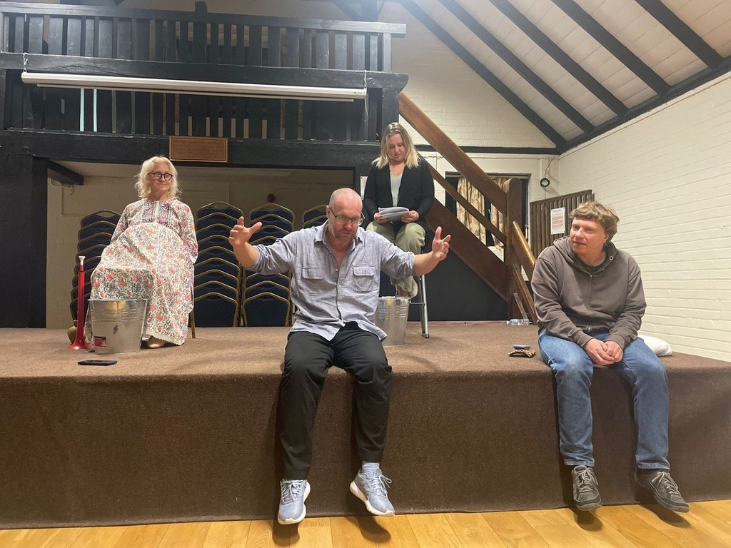 Dmitry Turchaninov's company in rehearsal in a village hall: actors on a low stage, one gesturing as he speaks, others watching