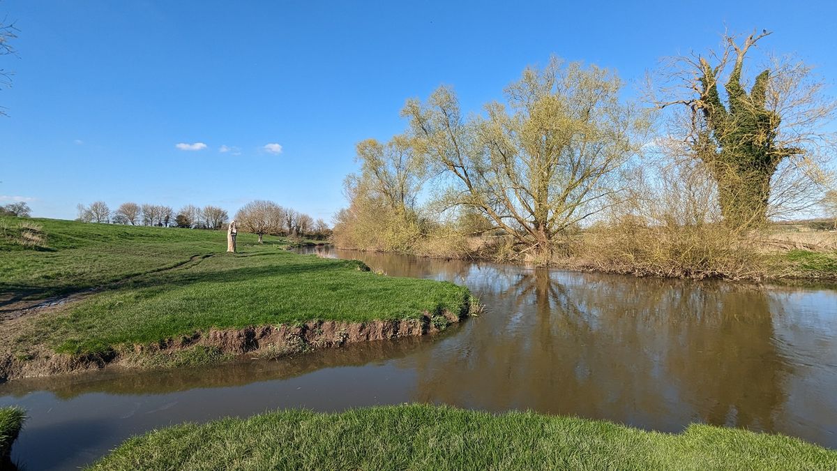 The River Cam winding through flat green Grantchester Meadows under a blue sky